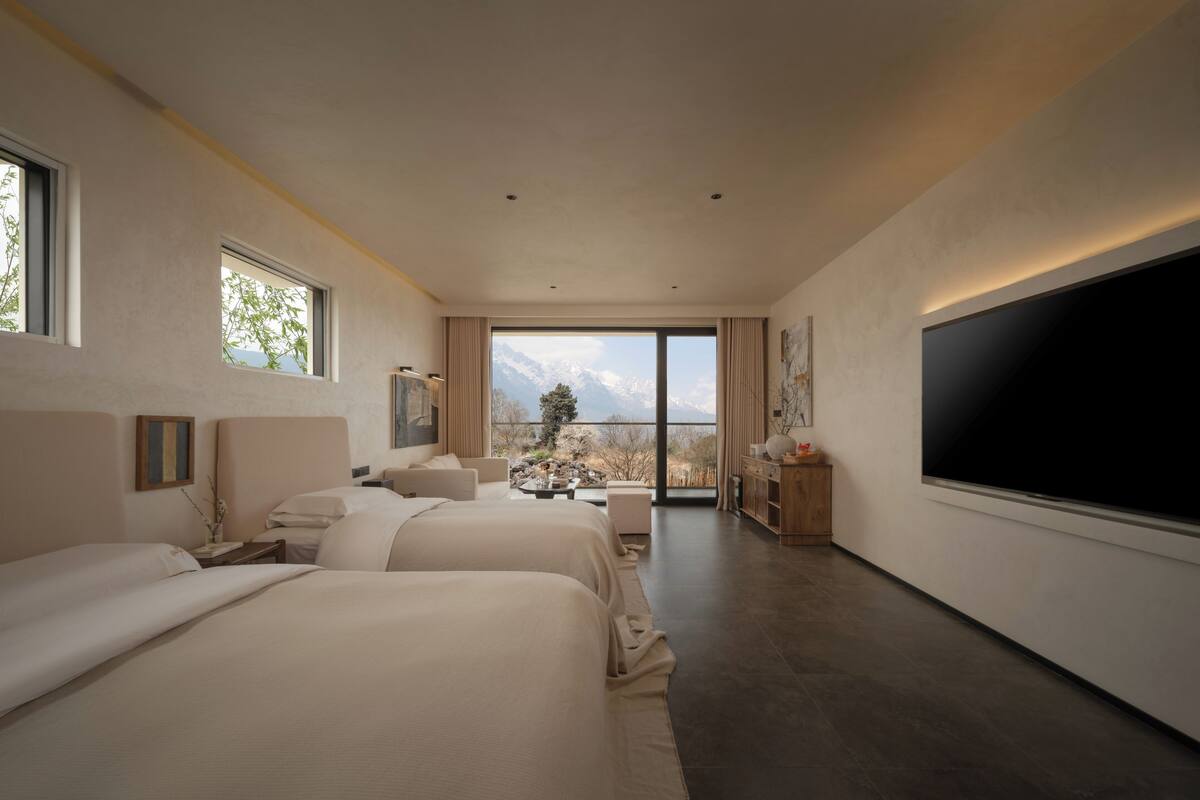 A modern hotel room with two beds, a large TV, and a balcony with a mountain view.