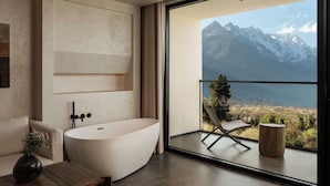 A modern bathroom with a freestanding bathtub, a wooden side table, and a view of mountains through a large window.
