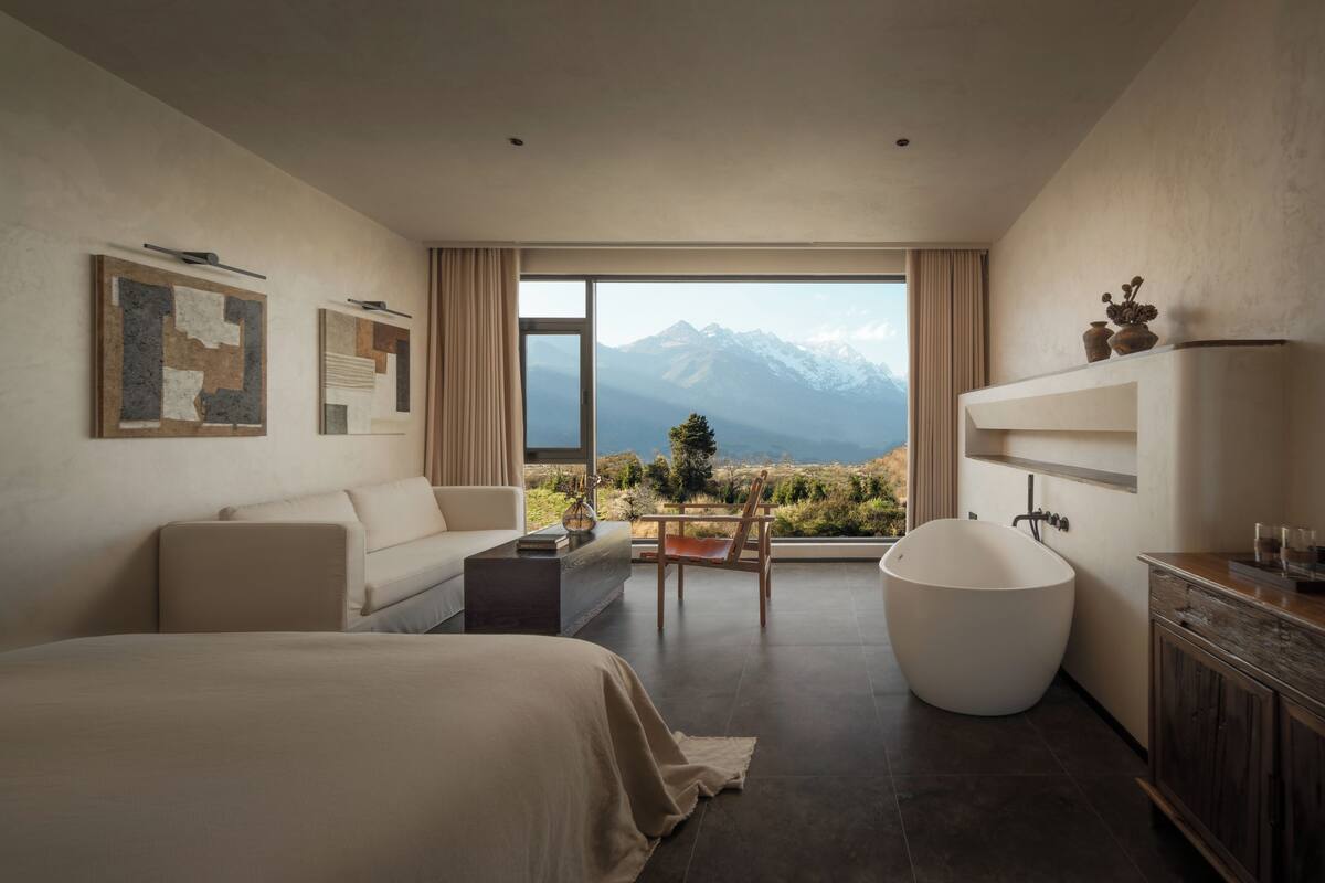 A modern bedroom with a large bed, a bathtub, and a view of mountains.