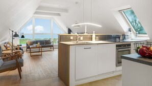 A modern loft apartment with a large skylight, a kitchen with a central island, and a cozy seating area with a view of the outdoors.