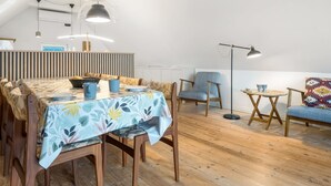 A modern loft-style room with a dining area, a seating area, and a high ceiling with exposed beams.