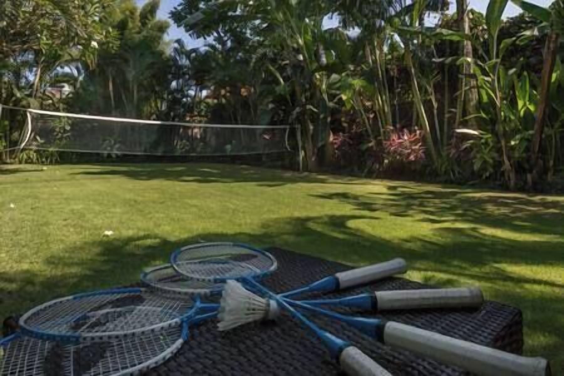 Uma quadra de badminton com rede, cercada por vegetação exuberante e palmeiras.