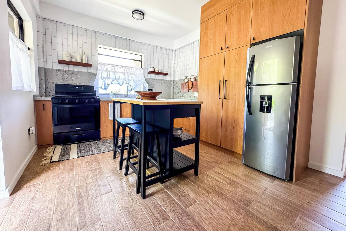 A modern kitchen with wooden cabinets, a stainless steel refrigerator, and a black countertop.