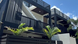 Un immeuble moderne à deux étages, doté d’un balcon, d’un escalier et d’une entrée fermée par un portail.