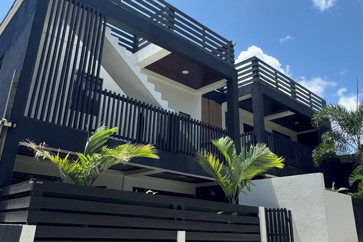 A modern two-story building with a balcony, a staircase, and a gated entrance.