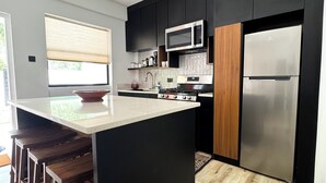Une cuisine moderne avec des meubles noirs, un réfrigérateur en acier inoxydable, un four à micro-ondes et un îlot central en bois doté de tabourets.
