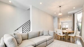 A modern living room with a sectional sofa, a dining area with a wooden table and chairs, and a staircase with a black railing. - NEW! Stylish 3BD/2.5BTH w/parking! United Center! (Chicago)