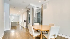A modern kitchen with white cabinets, a central island, and a dining area with a round wooden table and white chairs. - NEW! Stylish 3BD/2.5BTH w/parking! United Center! (Chicago)
