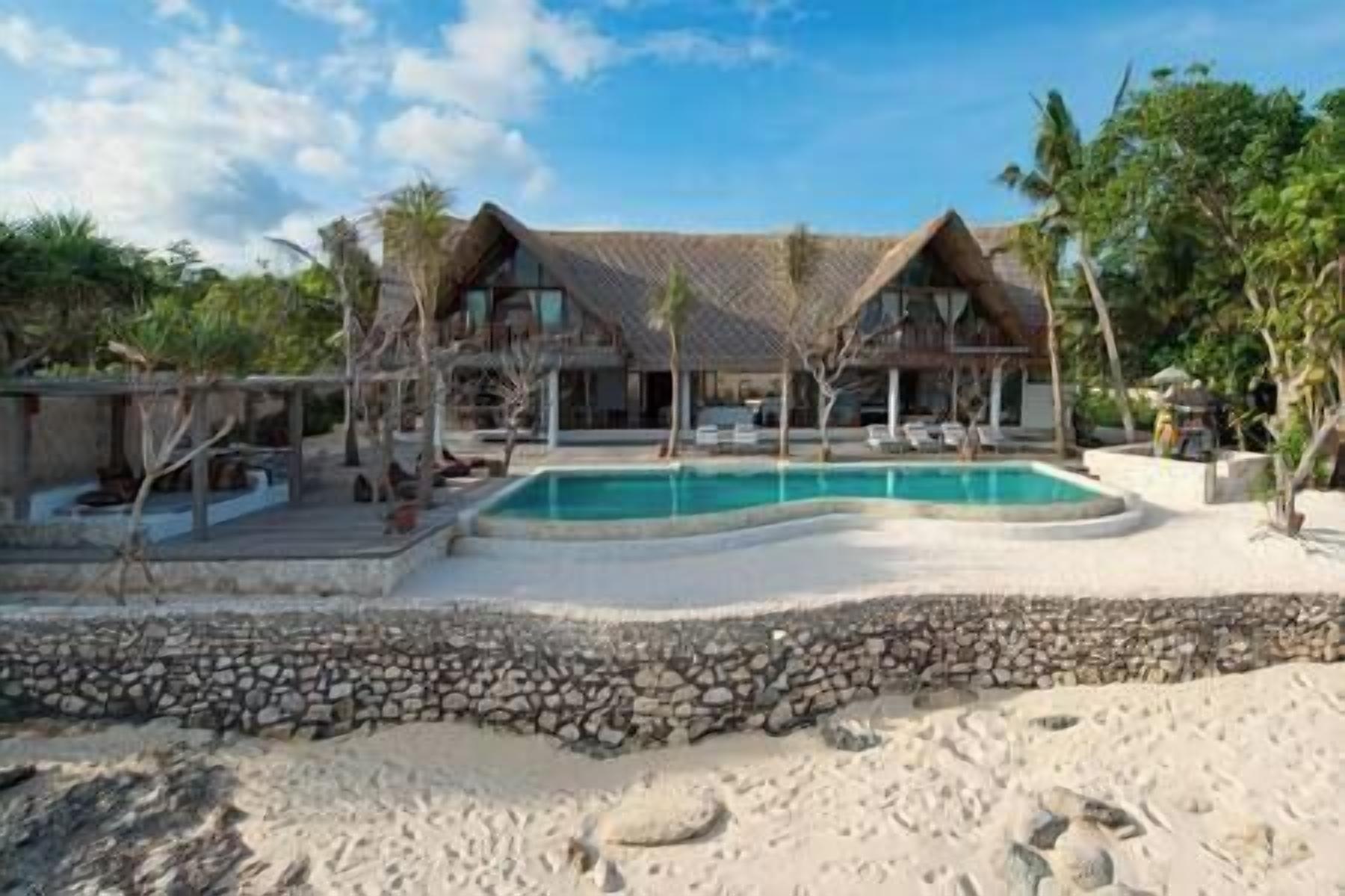 A resort with a pool, a stone wall, and a thatched-roof building.