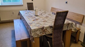 A dining area with a table covered in a floral tablecloth, surrounded by wooden chairs and benches.