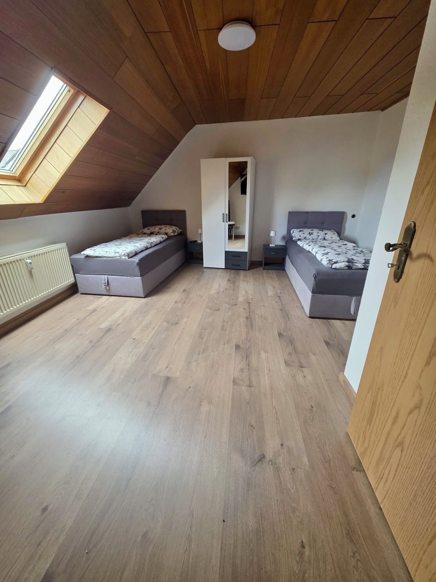 A bedroom with two beds, a wardrobe, a radiator, and a skylight.
