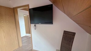A room with a flat-screen TV mounted on the wall, a wooden ceiling, and a light-colored chair.