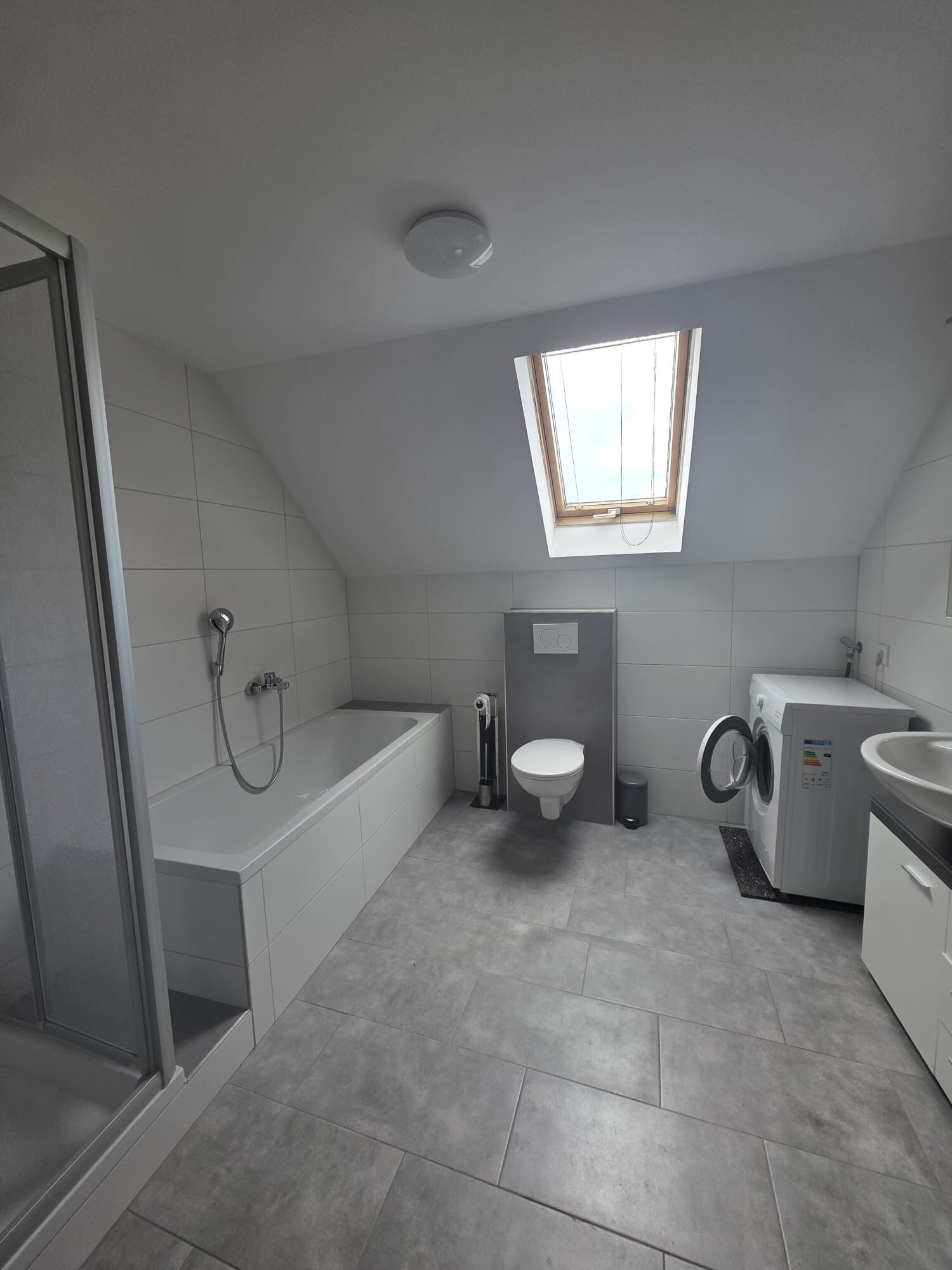 A modern bathroom with a skylight, a bathtub, a toilet, a washing machine, and a sink.