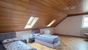 A bedroom with a sloped ceiling, wooden flooring, a bed with a patterned bedspread, a bedside table, and a radiator.
