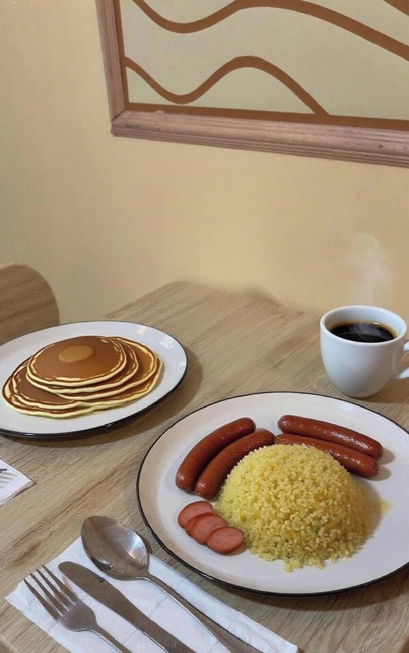 A breakfast setting with pancakes, sausages, couscous, and a cup of coffee on a wooden table.