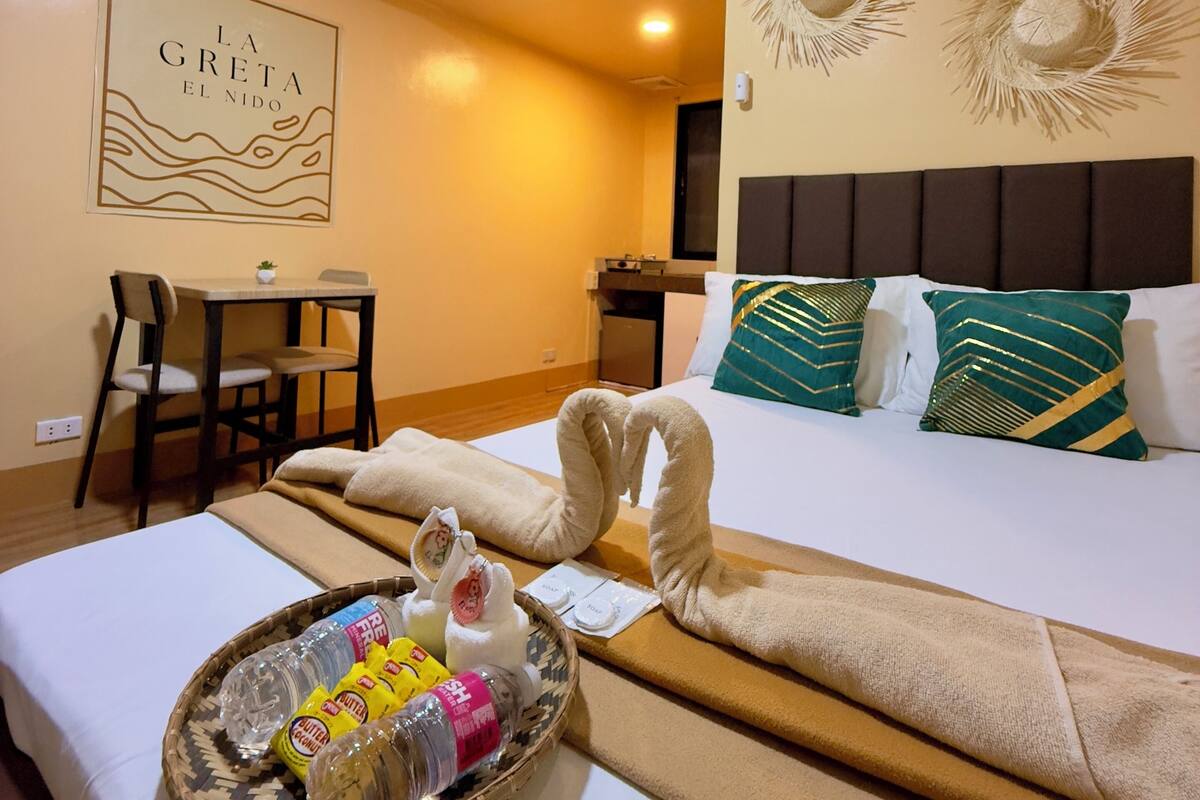 Habitación de hotel con cama, escritorio y silla. Hay una bandeja con artículos de aseo sobre la cama.