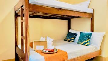 Una cama litera con estructura de madera, ropa de cama blanca y almohadas decorativas. Hay una bandeja con un pañuelero y un pequeño objeto sobre la cama.