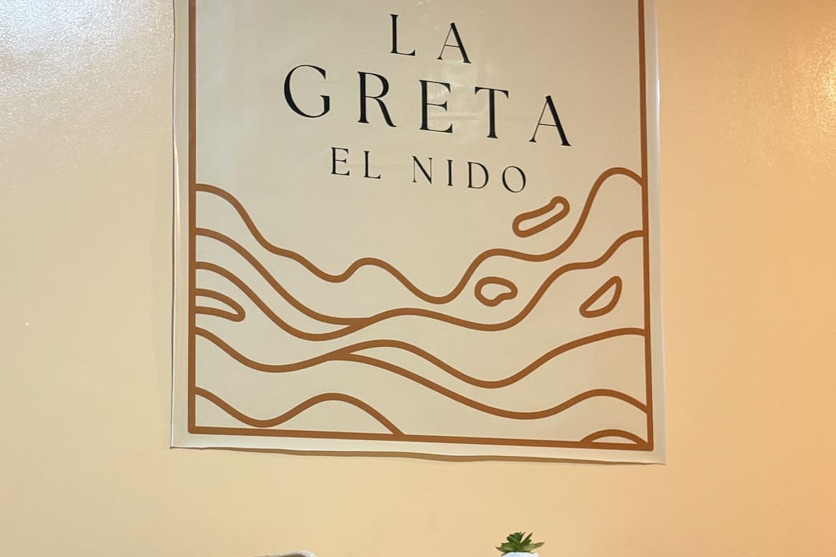 Un letrero enmarcado con texto, una pequeña mesa con sillas y una planta en maceta en la pared.