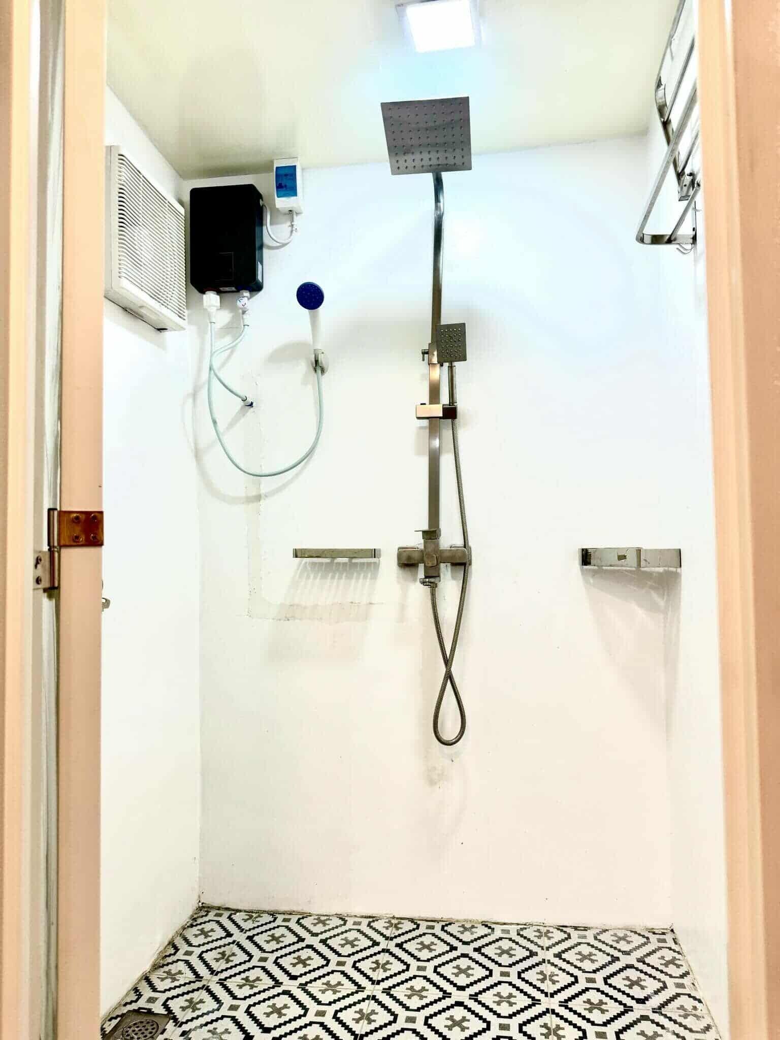 Un baño pequeño con azulejos, un cabezal de ducha manual, un grifo empotrado y un panel de control.