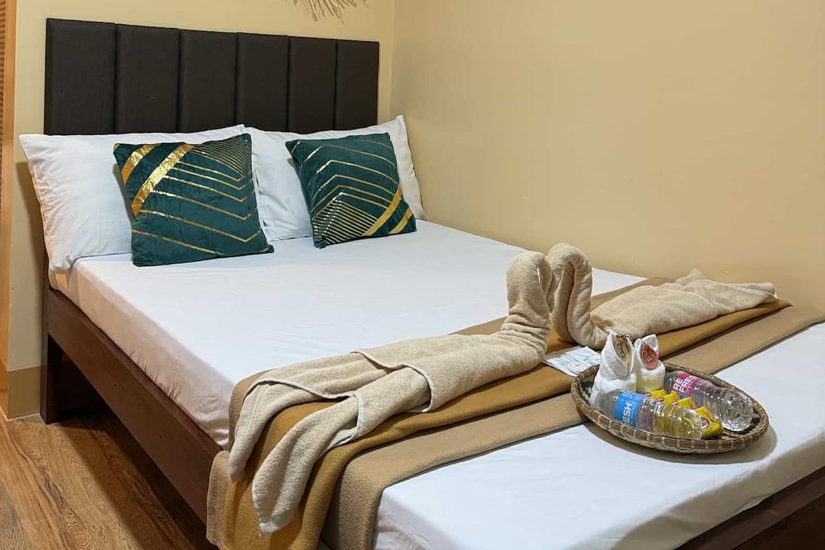 Una cama bien hecha con cabecera, dos obras de arte decorativas en la pared y una bandeja con artículos de aseo sobre la cama.