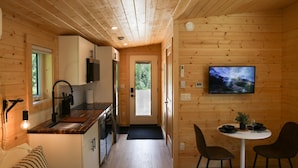 A compact wooden cabin with a kitchen, dining area, and a television mounted on the wall. - Arctic Lodge - Alpha Mountain Loding (Revelstoke)