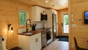 A compact kitchen with wooden walls, a built-in microwave, a stainless steel refrigerator, and a wooden countertop. - Arctic Lodge - Alpha Mountain Loding (Revelstoke)