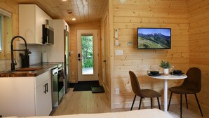 Ein kompaktes Ferienhäuschen mit Küche, Essbereich und einem an der Wand befestigten Fernseher.