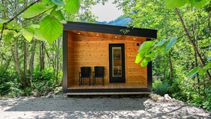 Eine Holzhütte mit zwei Stühlen und einer Tür, umgeben von dichtem Wald.