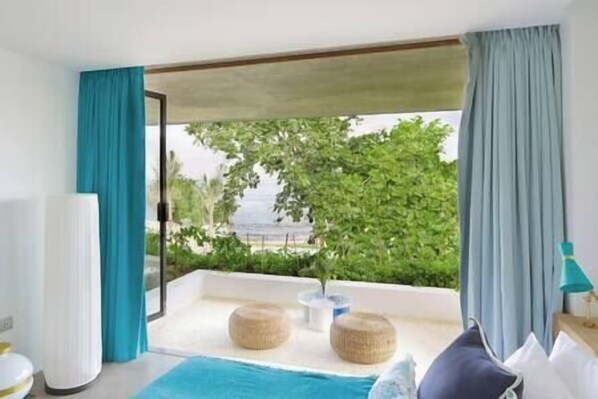 A room with a large window, a view of greenery, a white air conditioner, and a blue rug.
