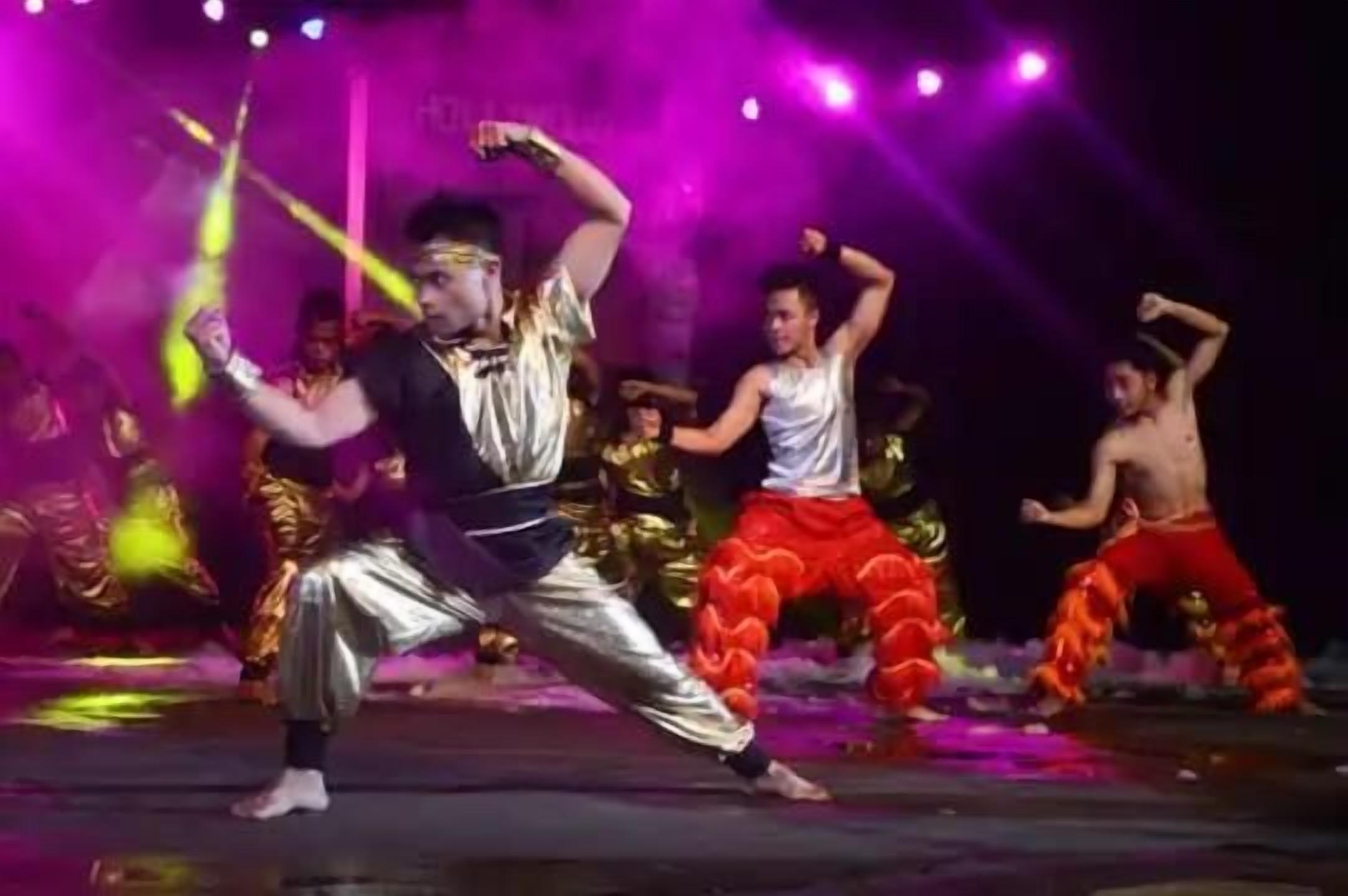 A group of dancers performing on a stage with bright stage lighting.