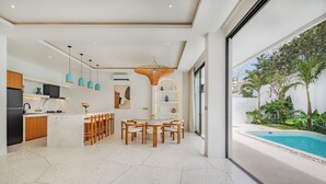 Una cocina moderna con una isla central, luces colgantes y vistas a una piscina.