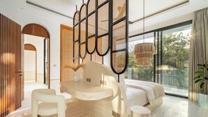 Un dormitorio moderno con un ventanal grande, un tocador curvo, una cama y una zona de estar.