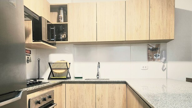 A compact kitchen with wooden cabinets, a stainless steel refrigerator, a microwave, and a built-in oven. - A HOME AWAY FROM HOME (Lima)