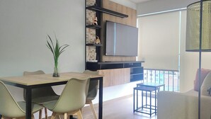 A modern living room with a dining area, a flat-screen TV mounted on a wooden wall, a sofa, and a floor lamp. - A HOME AWAY FROM HOME (Lima)
