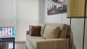 A living room with a sofa, a coffee table, and a floor lamp. There is a painting on the wall and a window with a view of buildings. - A HOME AWAY FROM HOME (Lima)