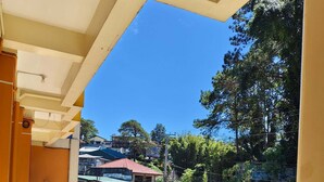 A balcony with patterned floor tiles, a metal railing, and a view of a street with buildings and trees. - Sukhavati Inn (Baguio)
