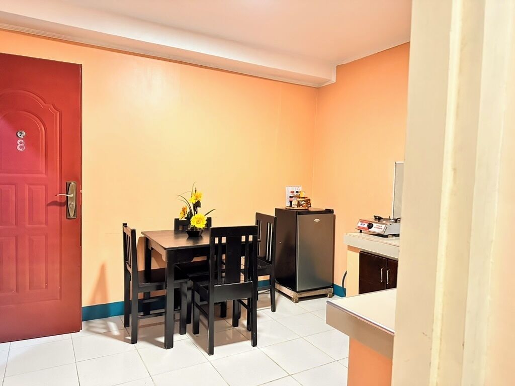 Una cocina compacta con una mesa de comedor, sillas, un refrigerador y una pequeña encimera.