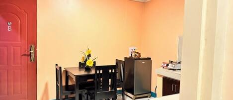 Una cocina compacta con una mesa de comedor, sillas, un refrigerador y una pequeña encimera.