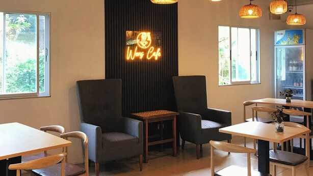 A modern cafe interior with multiple tables and chairs, warm lighting, and a neon sign reading "Wong Cafe". - Sukhavati Inn (Baguio)