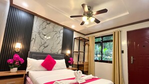 A hotel room with a bed, a ceiling fan, a window with curtains, a red door, and a wall with a marble-like pattern. - Sukhavati Inn (Baguio)
