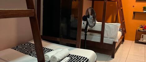 A room with two bunk beds, a fan, a TV on the wall, and a small shelf with items.