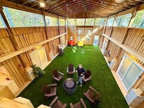 Un espace intérieur avec des murs en bois, une pelouse artificielle verte et un coin salon central avec des chaises et une table.