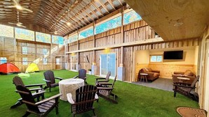 An indoor space with wooden walls, a green artificial turf area, and several Adirondack chairs.