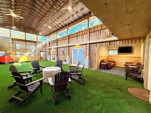 An indoor space with wooden walls, a green artificial turf area, and several Adirondack chairs.