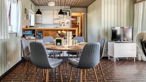 Un comedor con una mesa redonda, sillas grises tapizadas y un televisor sobre un mueble.