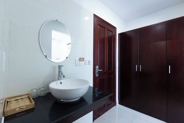 Un bagno moderno con un lavandino bianco, uno specchio rotondo e mobili contenitori in legno scuro.