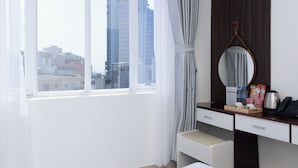 A hotel room with a large window, a wooden desk, a mirror, and a small table with toiletries. - Happy Home Boutique Hotel Vung Tau (Ho Chi Minh City)