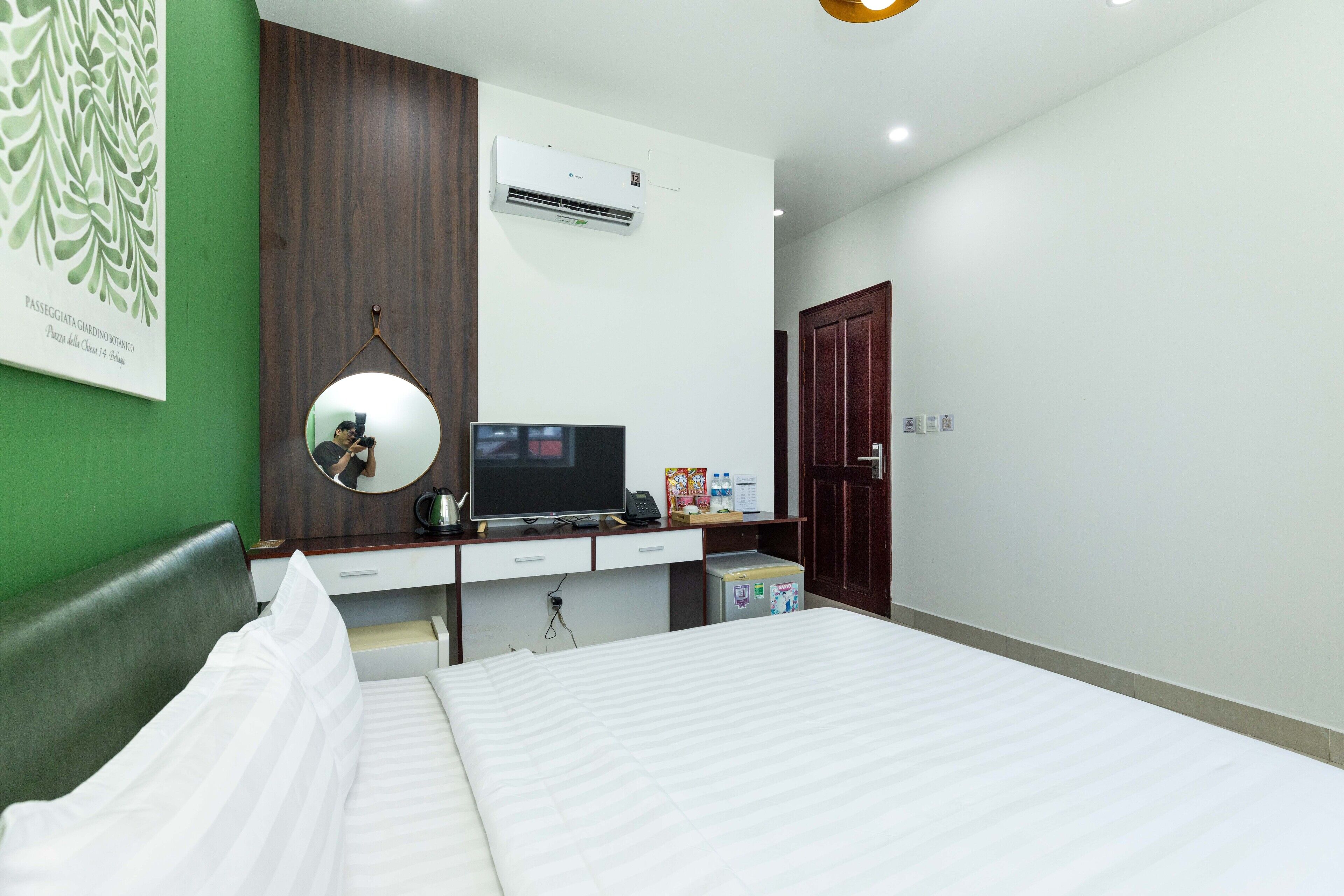 A hotel room with a bed, a desk with a computer, a mirror, and an air conditioner.