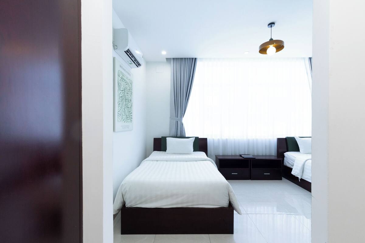 Ein modernes Hotelzimmer mit einem großen Bett, einem kleineren Bett, einem Schreibtisch und einem Fenster mit Vorhängen.