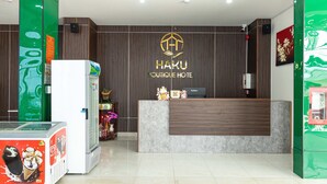 A reception area with a wooden reception desk, a green wall with a logo, and a white refrigerator. - Happy Home Boutique Hotel Vung Tau (Ho Chi Minh City)